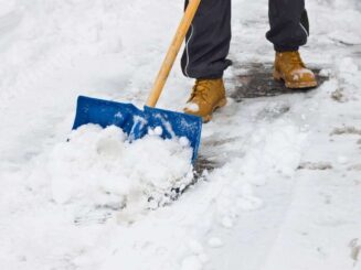 Snow removal service with snow shovel and boots on snowy driveway, winter landscaping cleanup.