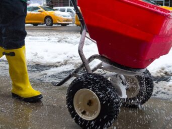 Worker spreading salt on an icy commercial sidewalk in winter.